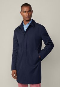 Marineblauer Mantel mit einem klassischen Kragen, zwei seitlichen Taschen und geradem Schnitt. Hergestellt aus einem glatten, leichten Stoff.