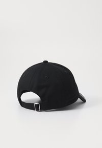 Casquette en coton noir avec une visière courbée, sangle ajustable et un patch logo circulaire sur le côté. Tissu texturé avec des détails de couture.