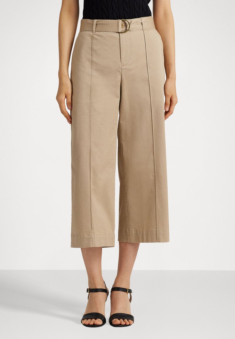 Light beige wide-leg trousers with a belt, featuring subtle seam details and a smooth texture. Paired with black strappy sandals.