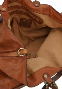 Borsa in pelle marrone con una morbida texture, ampio scomparto interno e fodera in tessuto. Presenta dettagli in metallo dorato e un'etichetta con logo.