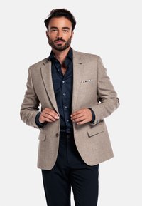 Beige wool blazer with a tailored fit, notch lapels, and two front pockets. Navy shirt underneath with button closure and contrasting accents.