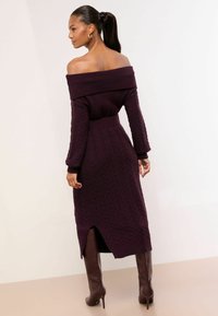 Off-shoulder strikket kjole i mørk lilla med kabelmønster, figursyet talje og midt-længde snit med en slids bagpå.