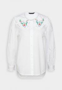 Camicia bianca con colletto arricciato, dotata di ricami floreali colorati. Maniche lunghe con polsini elastici e taglio dritto.