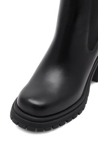 Czarny skórzany botek za kostkę z zaokrąglonym czubkiem, teksturowanymi bocznymi panelami oraz grubą, wytrzymałą podeszwą zapewniającą przyczepność. Gładkie wykończenie z delikatnym połyskiem.