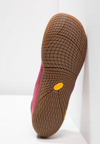 Zapato de ante rosa con una suela de goma marrón texturizada que presenta un patrón hexagonal y un logo amarillo de vibram en la parte inferior.