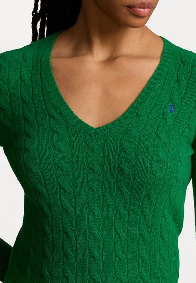 Zelený svetr s pleteným vzorem a výstřihem do V. Texturovaná tkanina má vyvýšený vzor kabelu. Malá modrá logo akcentace u výstřihu.