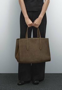 Bruine suède tote bag met twee lange handvatten, rechthoekige vorm, strakke lijnen en minimalistisch ontwerp. Gevoel met een zachte afwerking.
