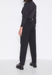 Svart denimjumpdräkt med en kroppsnära överdel och vida byxor, med uppvikta ärmar och två bakfickor. Slät textur och minimal sömnad.