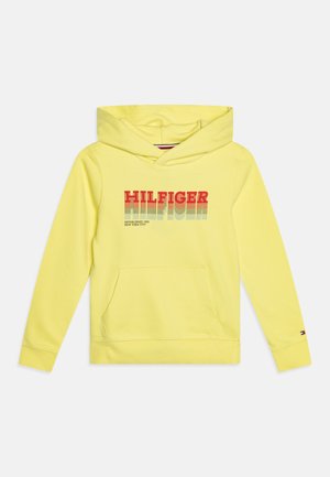 Żółta bluza z kapturem z kieszenią kangurka, na której znajduje się napis "HILFIGER" w czerwono-niebieskim gradientowym kolorze. Miękki materiał i ściągacze przy rękawach.