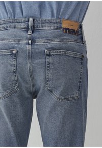 Helleblaue Denim-Jeans im klassischen Fünf-Taschen-Design, mit einem Leder-Patch mit der Aufschrift "mavi" am hinteren Bund.