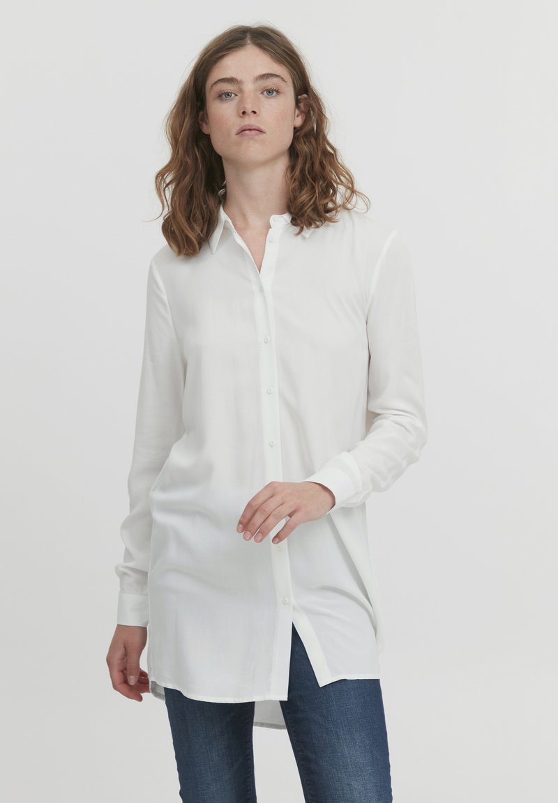 Camicia bianca con colletto, maniche lunghe e vestibilità comoda. Realizzata in tessuto morbido, presenta un orlo curvo e bottoni frontali.