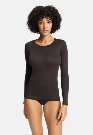 Woman with curly hair wearing a fitted long-sleeve dark brown top and matching underwear against a plain white background.