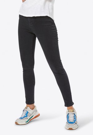 Jeans neri skinny con una texture liscia, vita alta e una silhouette aderente, abbinati a scarpe da ginnastica multicolori.