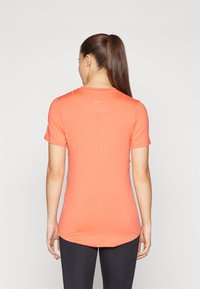 Kortermet, tettsittende sportskjorte i lys korall. Glatt tekstur, rund hals, har en liten Nike-logo på baksiden.