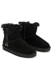 Botas de tobillo de ante negro con un cuello de piel de lujo, suela de goma plana y tira lateral con acento metálico. Textura suave y diseño robusto.