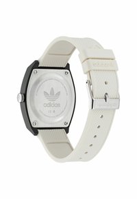 Montre avec un bracelet en silicone blanc et un boîtier hexagonal noir en acier inoxydable au dos. Présente le logo Adidas et un bracelet texturé pour une meilleure prise.