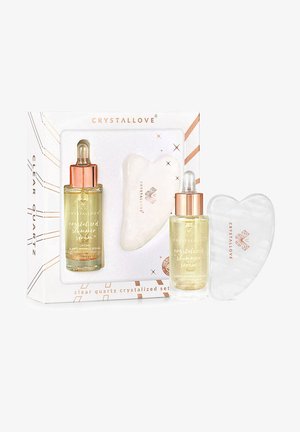 Kryształ górski w zestawie z przezroczystym narzędziem w kształcie serca oraz serum o złotym połysku w przezroczystej butelce z różowozłotymi akcentami.