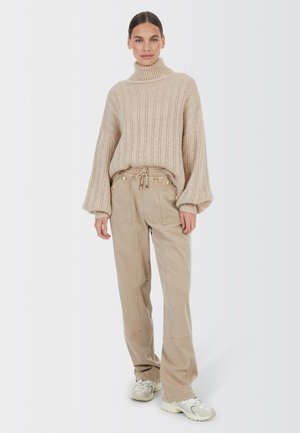 Beige knitted turtleneck sweater with ribbed texture and oversized sleeves, paired with light beige pants featuring drawstring and side pockets.