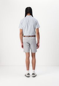 Chemise rayée à manches courtes en bleu et blanc, assortie avec un short gris clair. Détails de ceinture marron, chaussures de sport décontractées et chaussettes blanches.