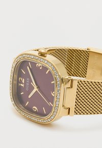 Arany színű hálós óra négyzet alakú bordó számlappal, arany órajelzőkkel és kristállyal díszített kerettel. Oldalsó kronográf található az állításhoz.