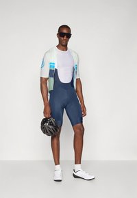 Cyklodres světlomodrý s krátkým rukávem a pruhy, tmavě modré návleky na nohy a černá přilba. Kombinováno s bílými sportovními botami.