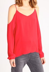 Rød, langærmet bluse med cold shoulder-design, v-hals og flydende stof. Har elastiske manchetter og en afslappet pasform.