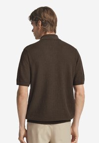 Braunes, strukturiertes Poloshirt mit kurzen Ärmeln und geripptem Kragen. Der Stoff hat ein erhabenes Muster und bietet einen lässigen Look.
