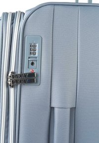 Maleta rígida de color azul claro con acabado texturizado, cerradura de combinación y logotipo de DKNY en los dobles cierres. Cuenta con un mango retráctil.