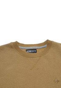 Ruskea puuvillapaita, jossa on teksturoitu neule, ribbikuvioitu kaula-aukko ja brodeerattu logo. Edessä on diagonaalinen ommeltu yksityiskohta.