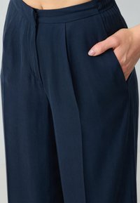 Marineblauwe wijde broek gemaakt van een zachte stof, met plooien aan de voorkant en zijzakken, voorzien van een elastische tailleband voor extra comfort.