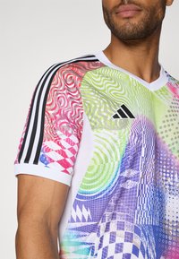 Colorful athletic shirt with a mix of spiral and geometric patterns in pink, green, and blue. Features black stripes on sleeves and Adidas logo.
