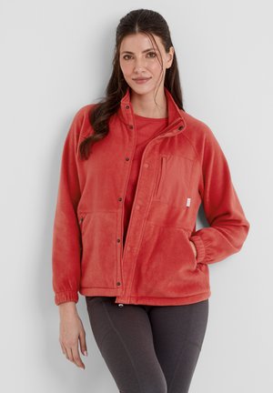 Fleece jacket in coral, featuring a zippered pocket, snap closures, and elastic cuffs. Worn over a matching top and paired with dark leggings.