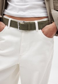 Roheline sametist vöö hõbedase pandlaga, mis on kantud valgete kõrge vöökohaga pükste peal, millel on ees taskud ja nähtavad õmbluse detailid.