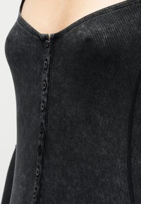 Μαύρο ριμπ αμάνικο τοπ με εφαρμοστή σχεδίαση, μεγάλο ντεκολτέ και σειρά από έξι μαύρα κουμπιά στο μπροστινό μέρος για κλείσιμο.