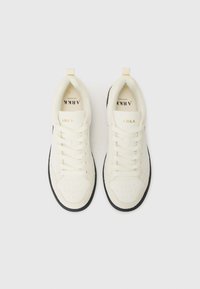 Zapatillas blancas con un acabado texturizado, que presentan una puntera perforada, cordones planos y una suela negra en contraste. Marca en dorado en la lengüeta.
