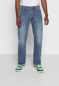 Světle modré džíny, rovný střih, s designem pěti kapes a kovovým kováním. Kombinované se zeleno-bílými teniskami.