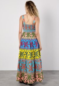 Robe maxi avec un corsage froncé, présentant des motifs vibrants en rose, bleu, jaune et vert. Design à volants avec des accents floraux et larges bretelles.