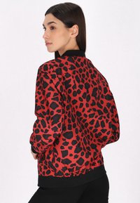 Giacca bomber con stampa leopardata rossa e nera, dotata di colletto e polsini in maglia, con una vestibilità ampia e vita elasticizzata.