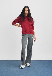 Mørkerød hettegenser med frontlomme og grå treningsbukser med sidestriper. Fullført med hvite og grønne joggesko. Blå teppegulv i bakgrunnen.