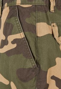 Camouflajebukser med en blanding av grønt og beige stoff, synlige lommer og en teksturert overflate, som viser et militærinspirert mønster.