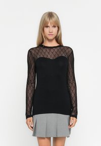 Black long-sleeve top featuring a sheer patterned mesh yoke with a sweetheart neckline. The body is solid black, paired with a grey pleated skirt.
