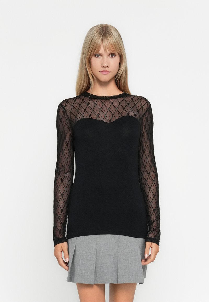 Black long-sleeve top featuring a sheer patterned mesh yoke with a sweetheart neckline. The body is solid black, paired with a grey pleated skirt.
