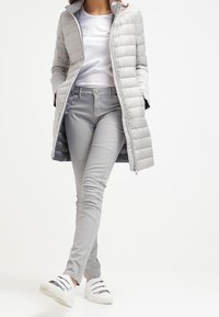 Jasnoszara kurtka puchowa o pikowanym wzorze, w połączeniu z dopasowanymi jasnoszarymi spodniami. Białe sneakersy z wieloma paskami. Proste, eleganckie linie.