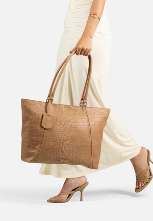 Borsa tote in pelle con stampa coccodrillo color tan, dotata di doppi manici e un tag. Presenta una forma strutturata e una consistenza liscia, ideale per l'uso quotidiano.