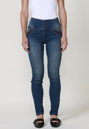 Jeans de mezclilla azul de cintura alta con cierre de tres botones, cinco bolsillos y costuras decorativas. Forma de pierna ajustada, textura suave.