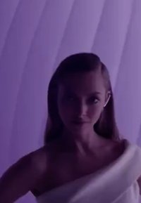 Vêtement en tissu blanc drapé, à texture douce, porté sur une épaule. Un dégradé subtil de tons violets en arrière-plan renforce l'intérêt visuel.