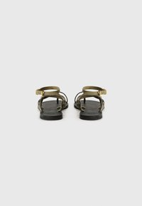 Sandali in suede verde con un design minimalista, dotati di suole nere e di una cinghia per la caviglia con fibbia dorata, aperti davanti e con fasce laterali.