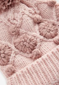 Strickmütze in Pink mit strukturierten Pom-Pom-Akzenten und Zopfmustern. Der gerippte Saum am Boden sorgt für Struktur und Details.