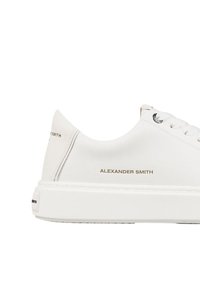 Sneaker bianco in pelle con suola spessa, dettagli testurizzati e lettering dorato sul lato che recita "ALEXANDER SMITH."