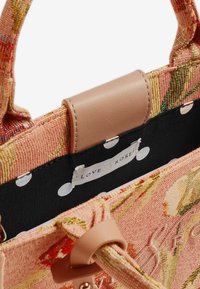 Borsa a motivo floreale in tessuto rosa testurizzato con manico in pelle beige liscia, dotata di una fodera a pois neri e etichetta.